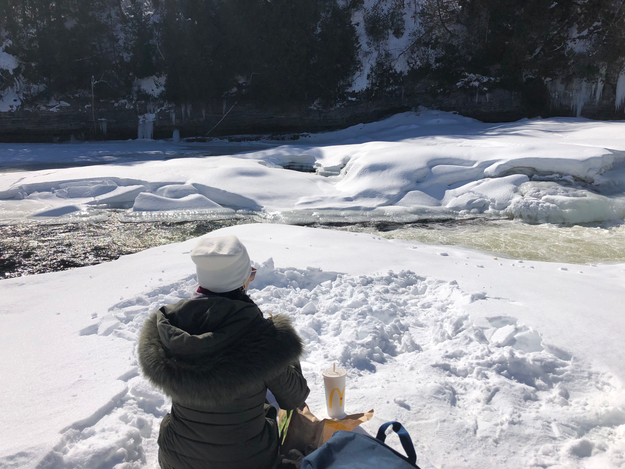 Girl sitting in snow facing partially frozen river