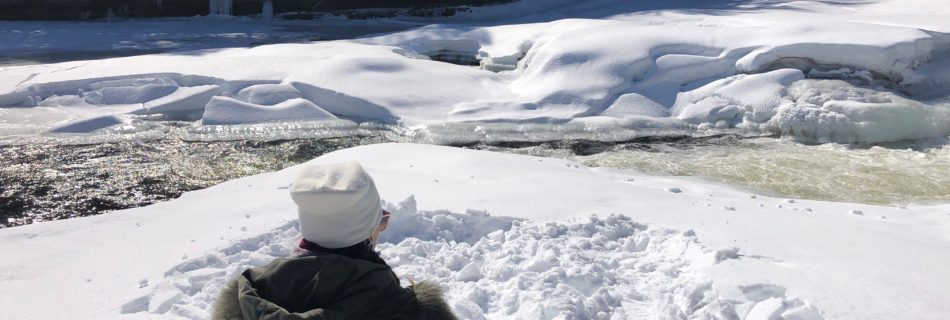 Girl sitting in snow facing partially frozen river